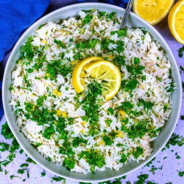 A bowl of easy Greek rice topped with chopped parsley and slices of lemon.