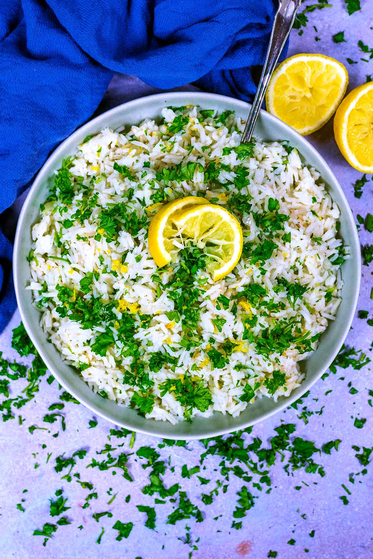 A large bowl of cooked rice, topped with chopped herbs and slices of lemon.