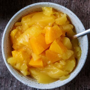 A bowl of orange jelly with chunks of peach in it.