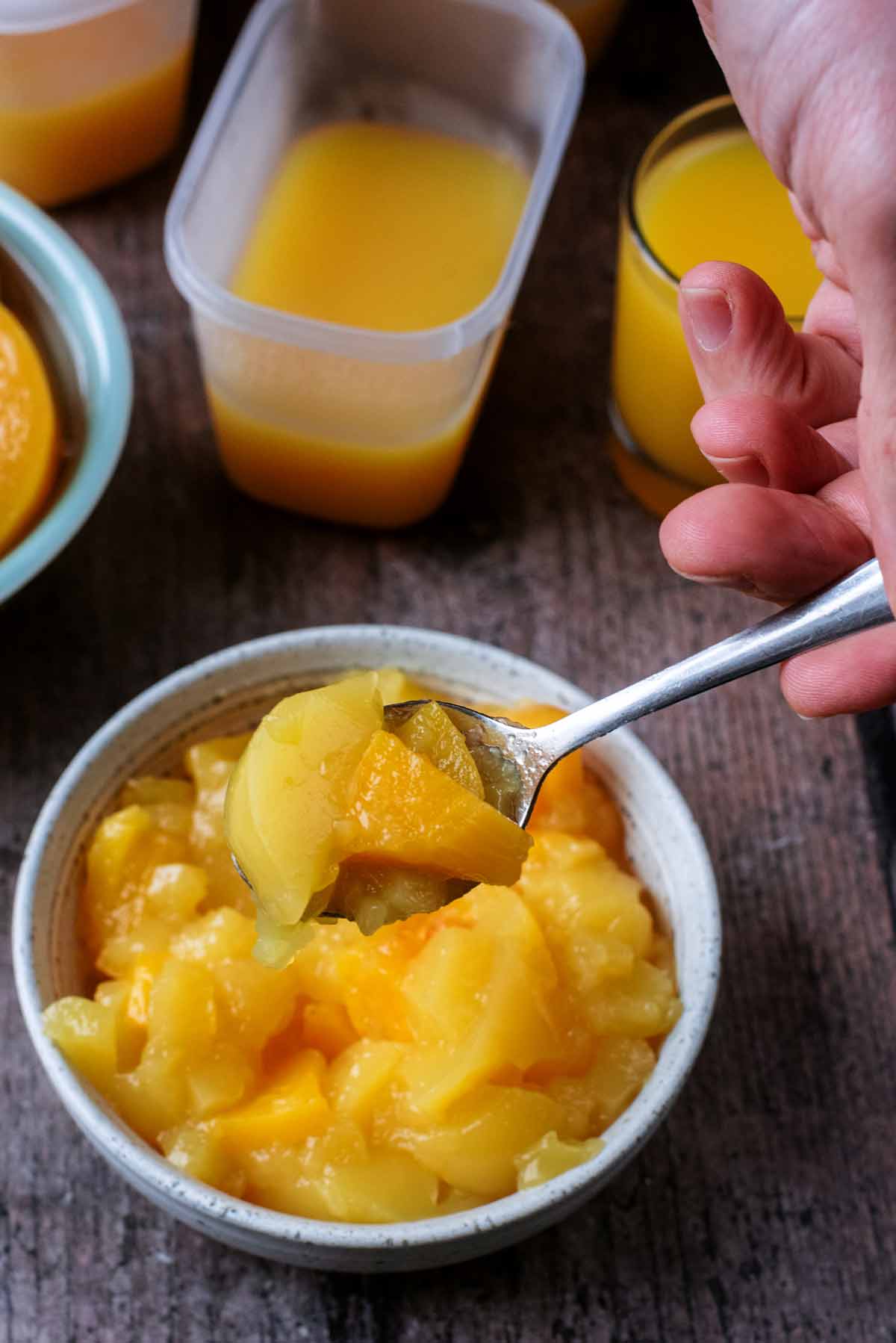 A spoon lifting some orange jelly from a bowl.
