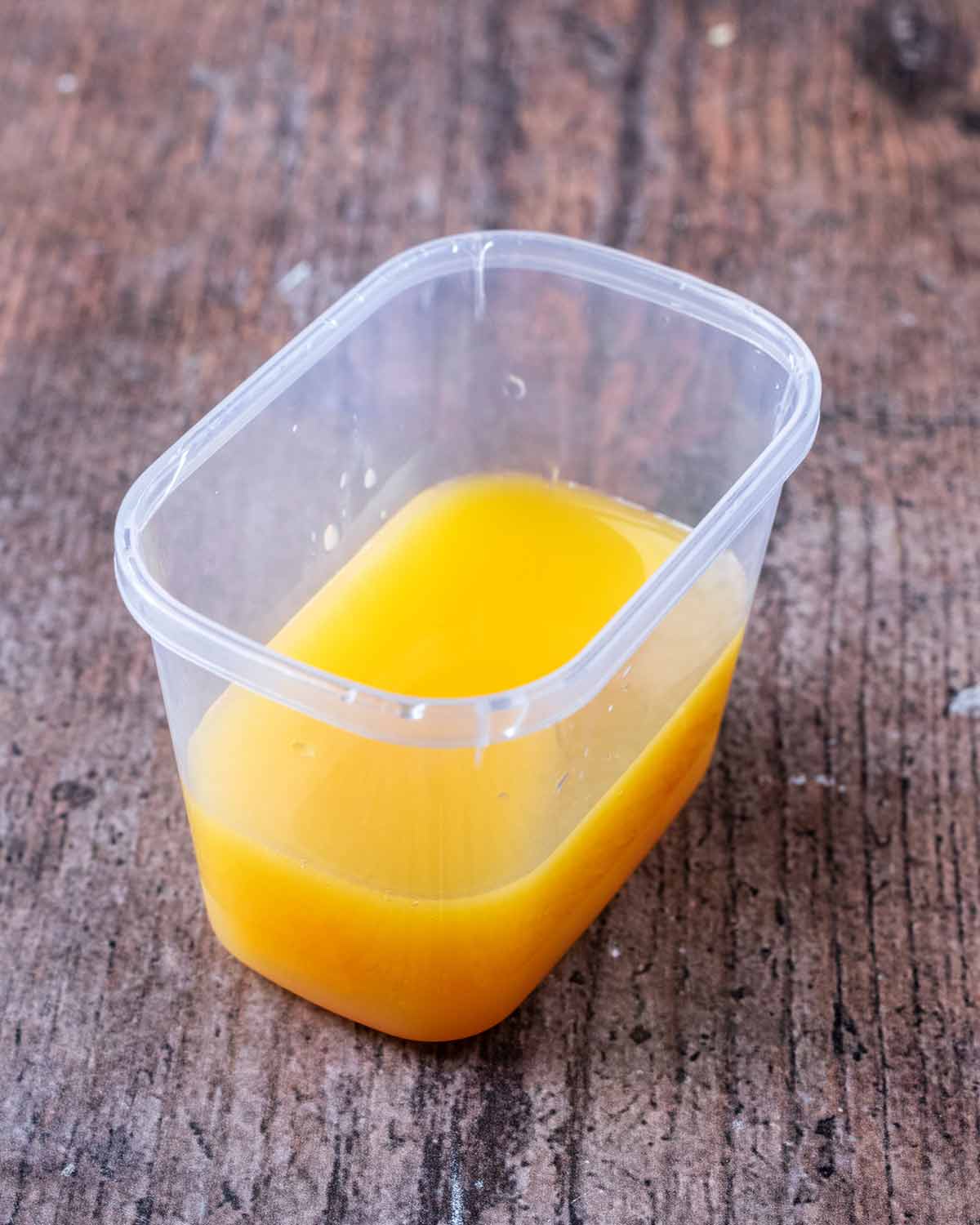 A small plastic tup containing liquid orange jelly.