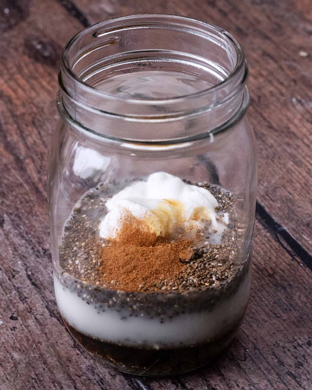 A glass jar containing chia seeds, milk, yogurt, maple syrup and cinnamon.