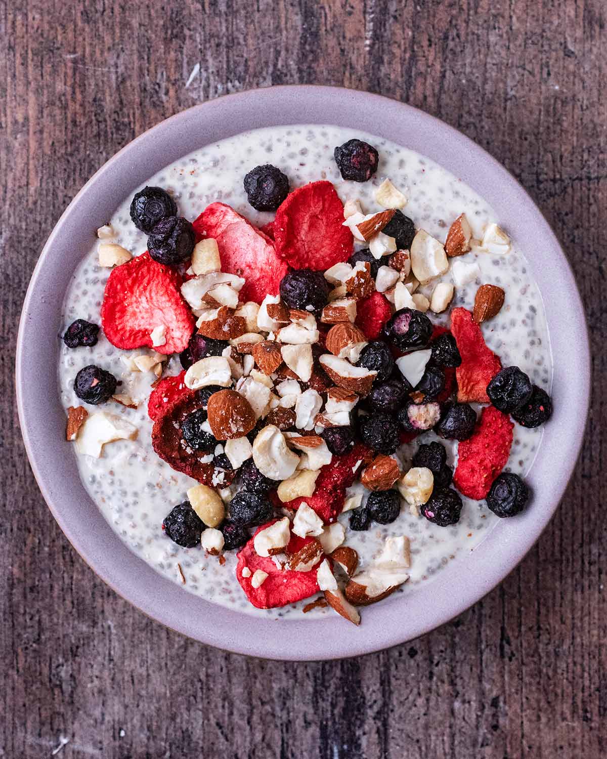 Chia pudding in a bowl with berries and crushed nuts.
