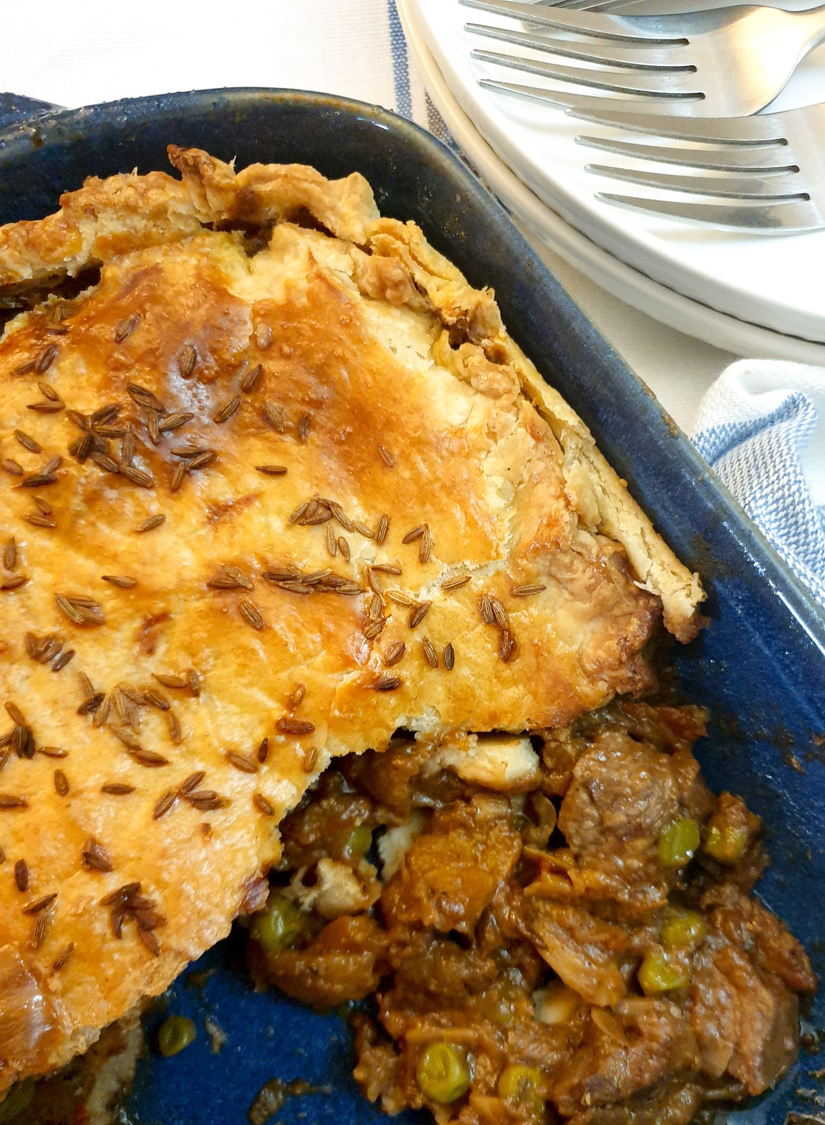 A shortcrust pie in a blue bowl with cooked lamb and peas spilling out.