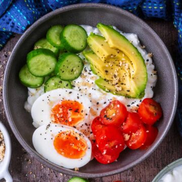 Cottage cheese bowl topped with boiled egg, sliced cucumber, avocado and tomato slices.