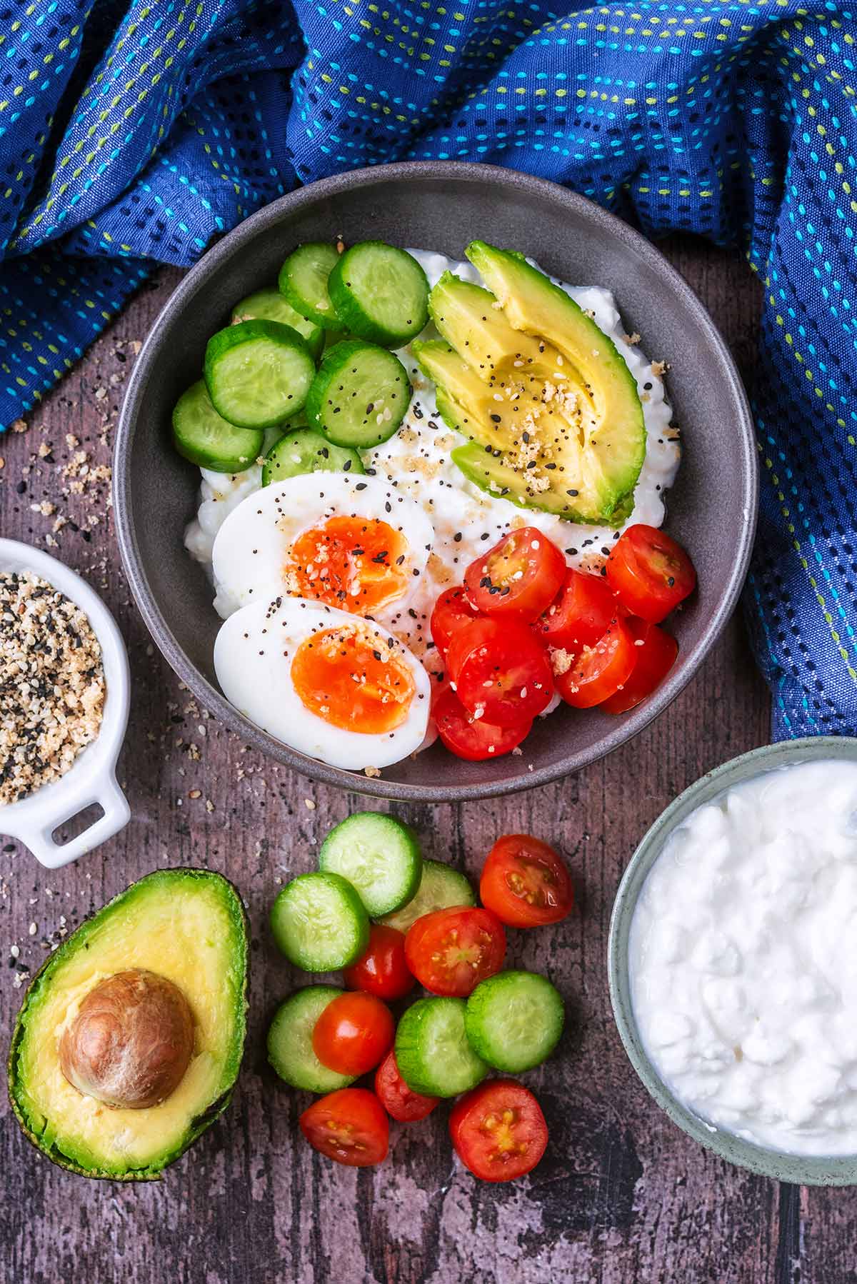 A bowl of cottage cheese , egg and salad next to more cottage cheese, cucumber and tomato slices.