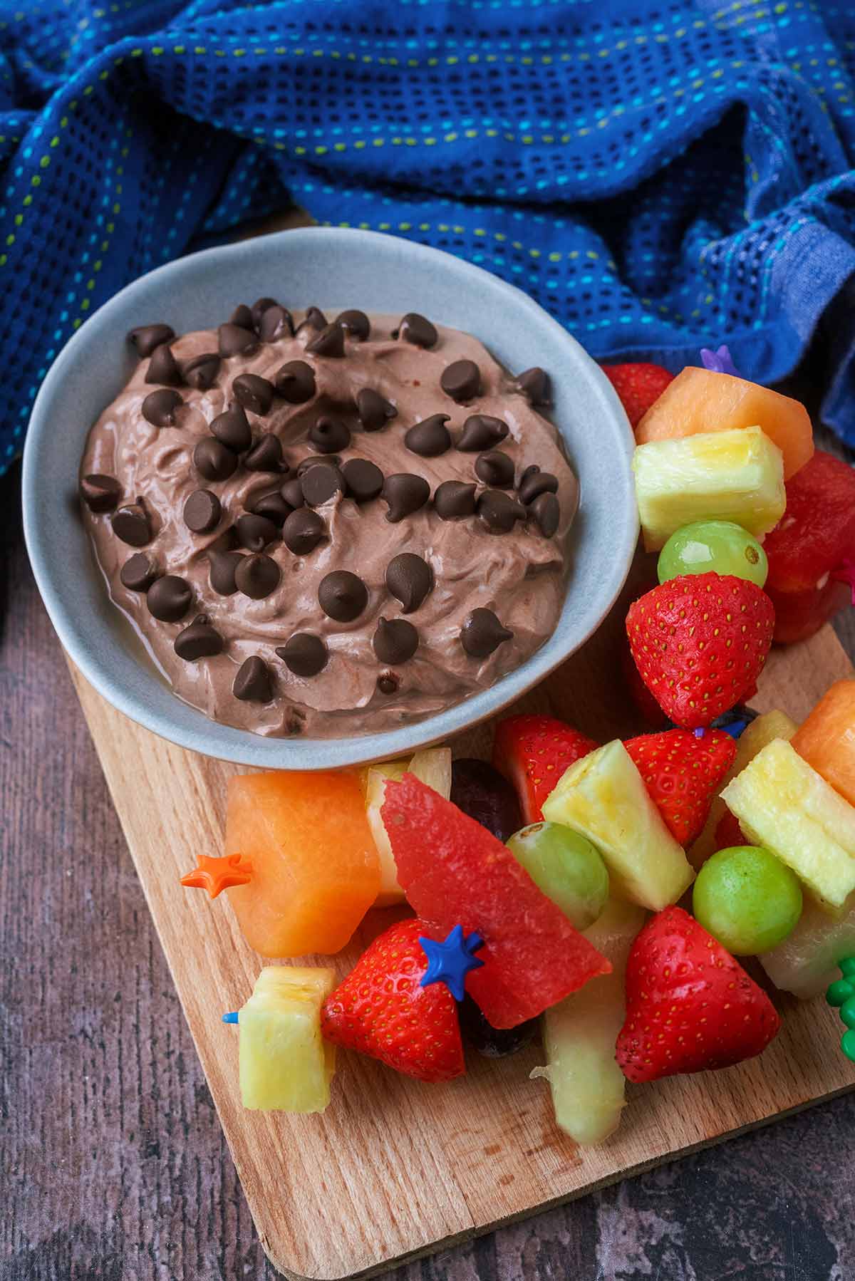 A bowl of chocolate dip next to small fruit skewers.