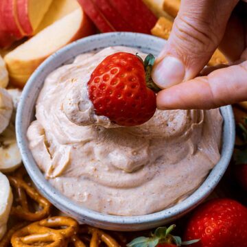 A strawberry being dipped into a bowl of peanut butter yogurt dip.