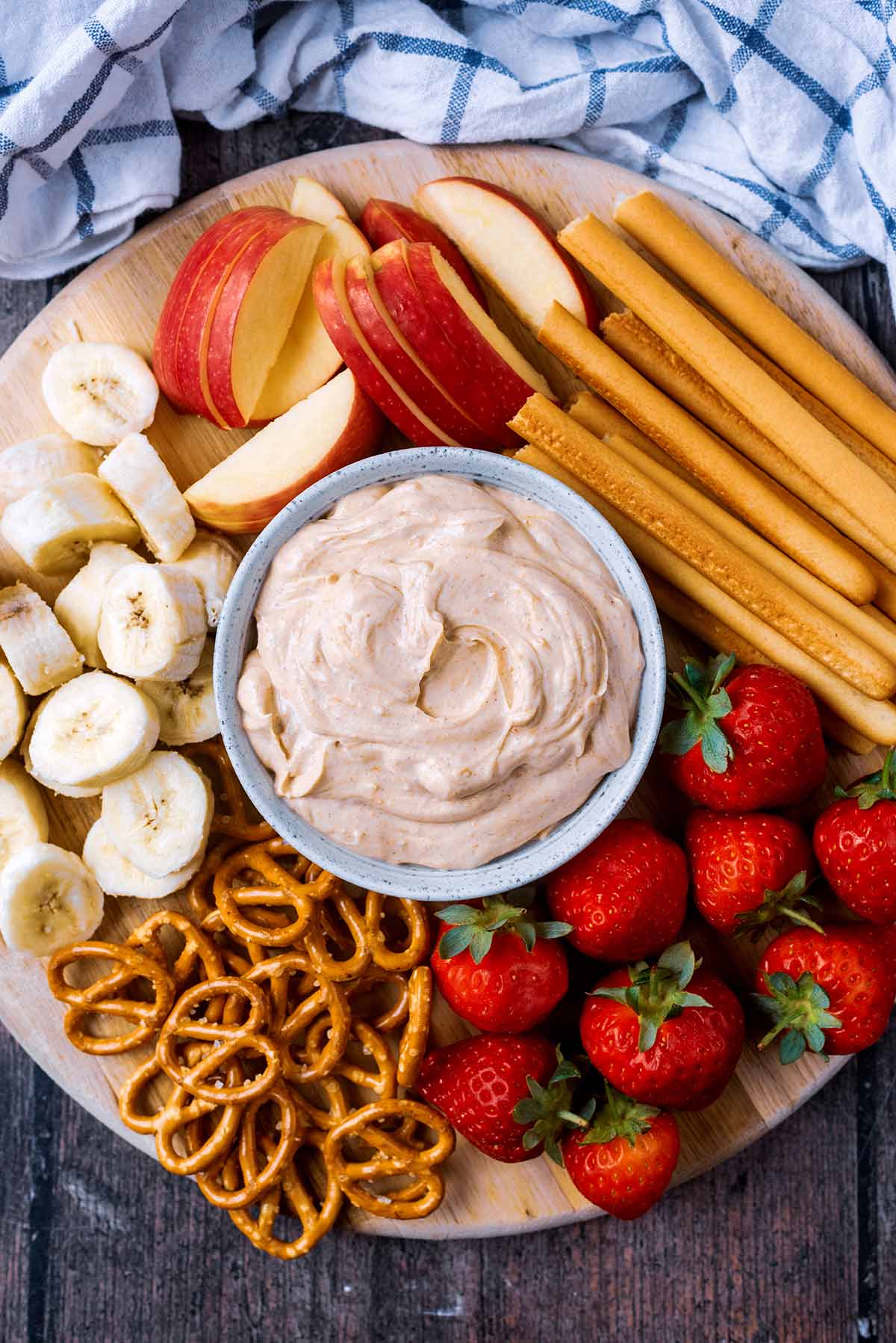 A bowl of dip surrounded by bread sticks, pretzels, strawberries, banana slices and apple slices.