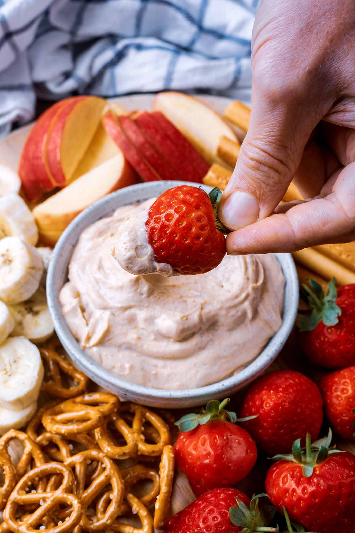 A hand dipping a strawberry into a yogurt dip.