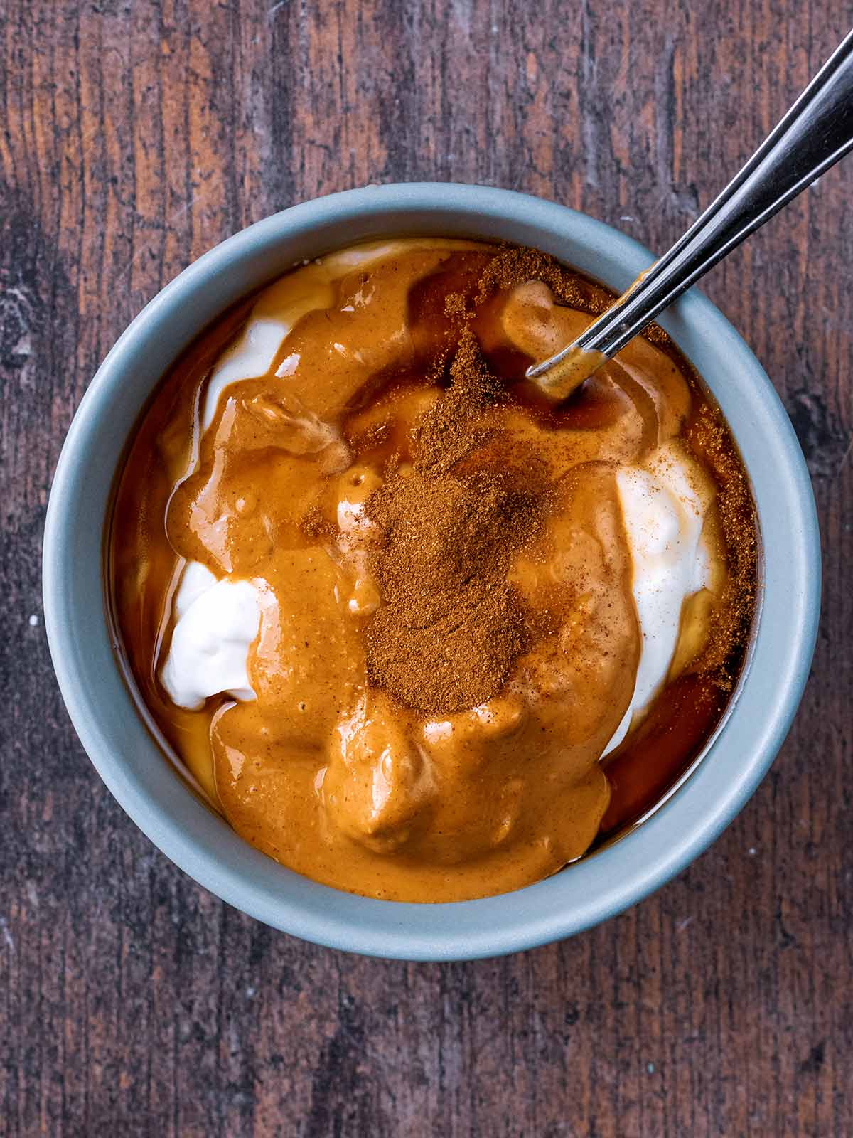 Yogurt, peanut butter, maple syrup and cinnamon in a bowl with a spoon.