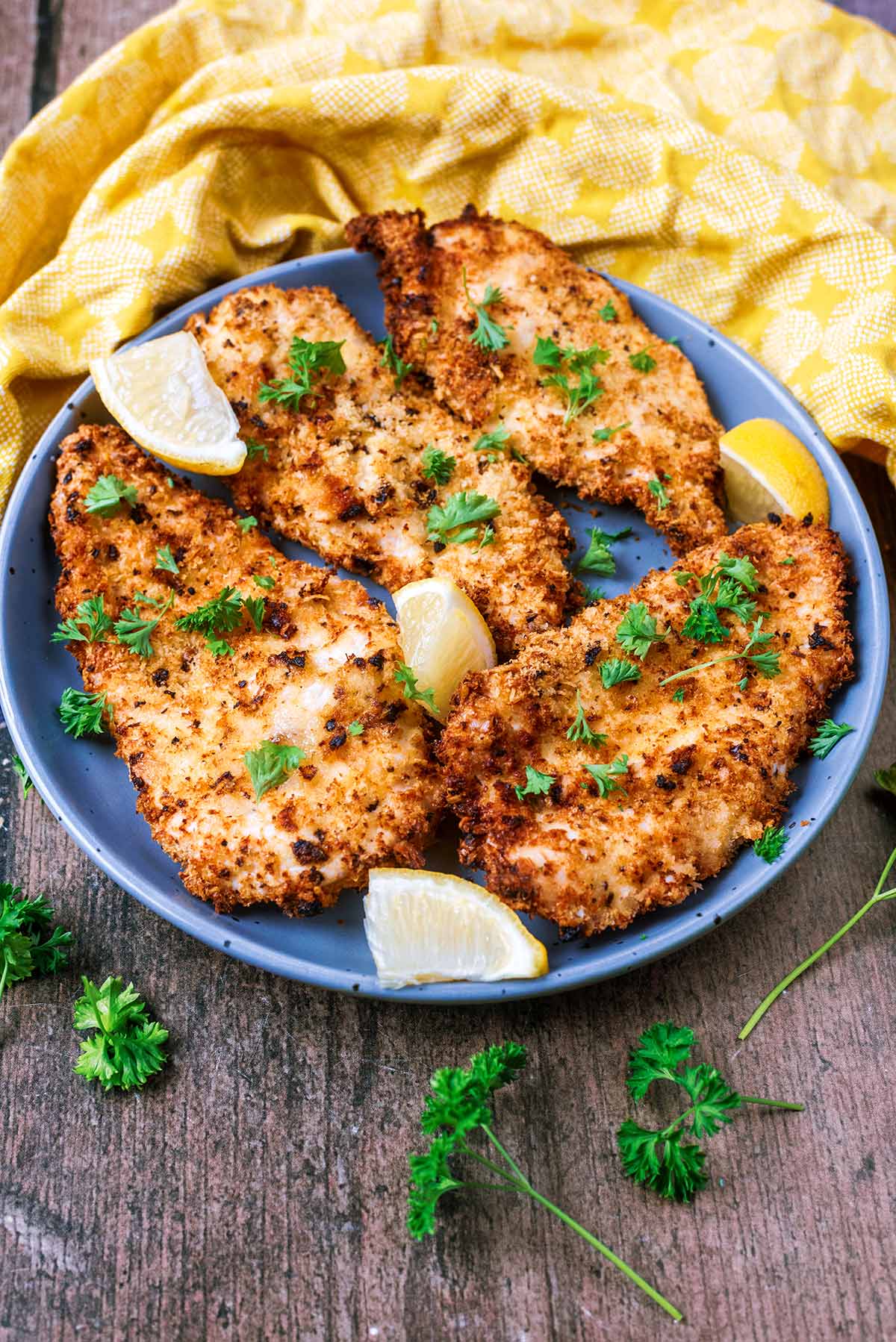 A plate of breaded chicken breasts with parsley and lemon wedges.