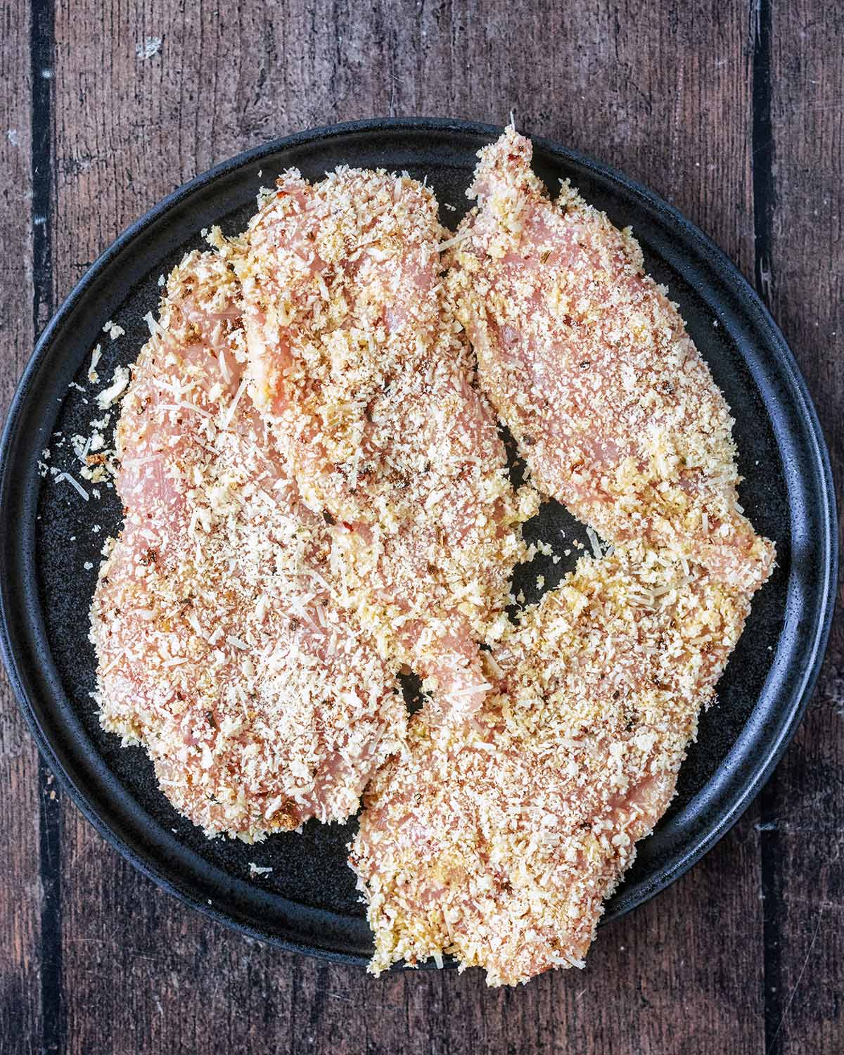 Chicken breasts coated in seasoned breadcrumbs on a plate.