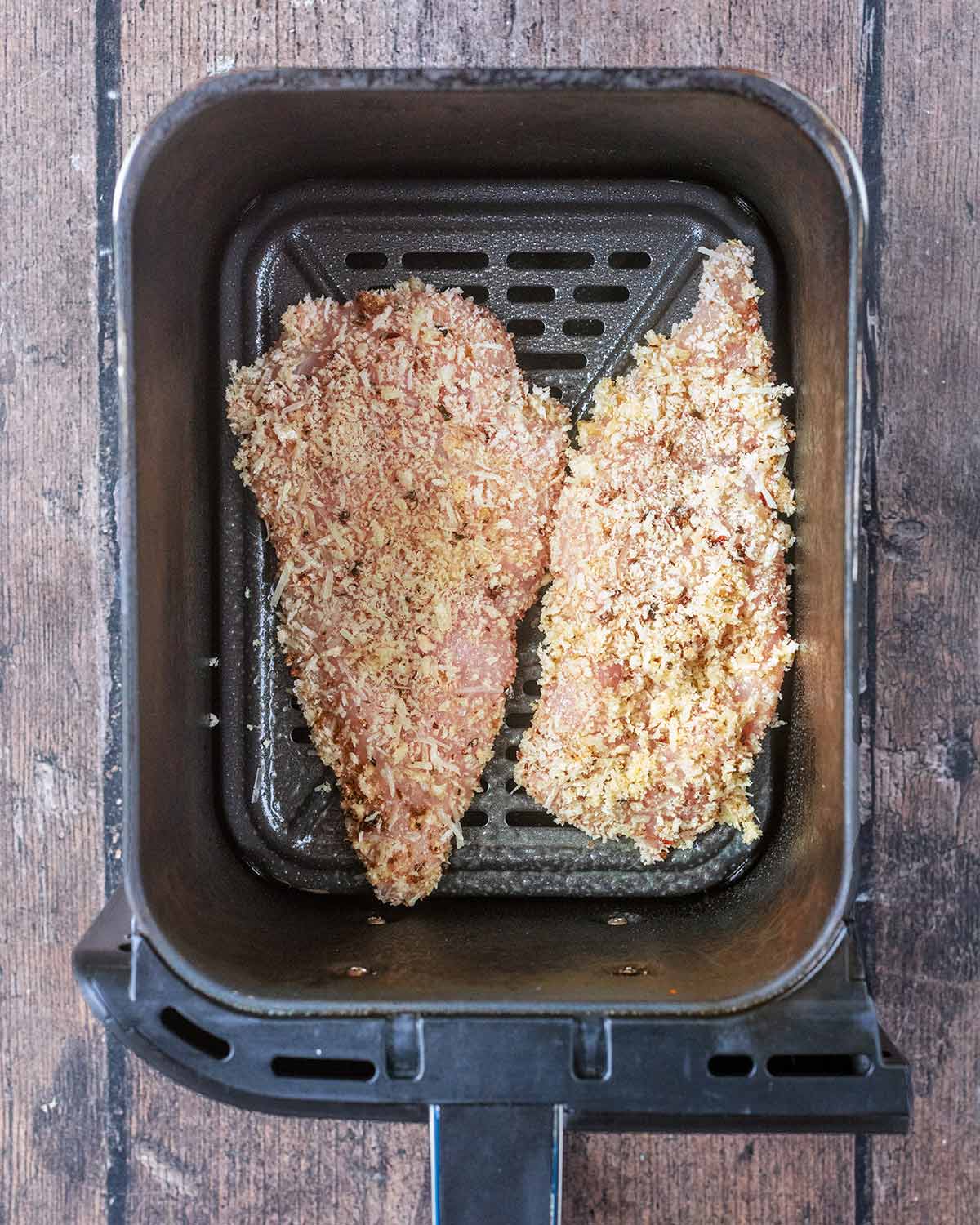 Breaded chicken breasts in an air fryer basket.