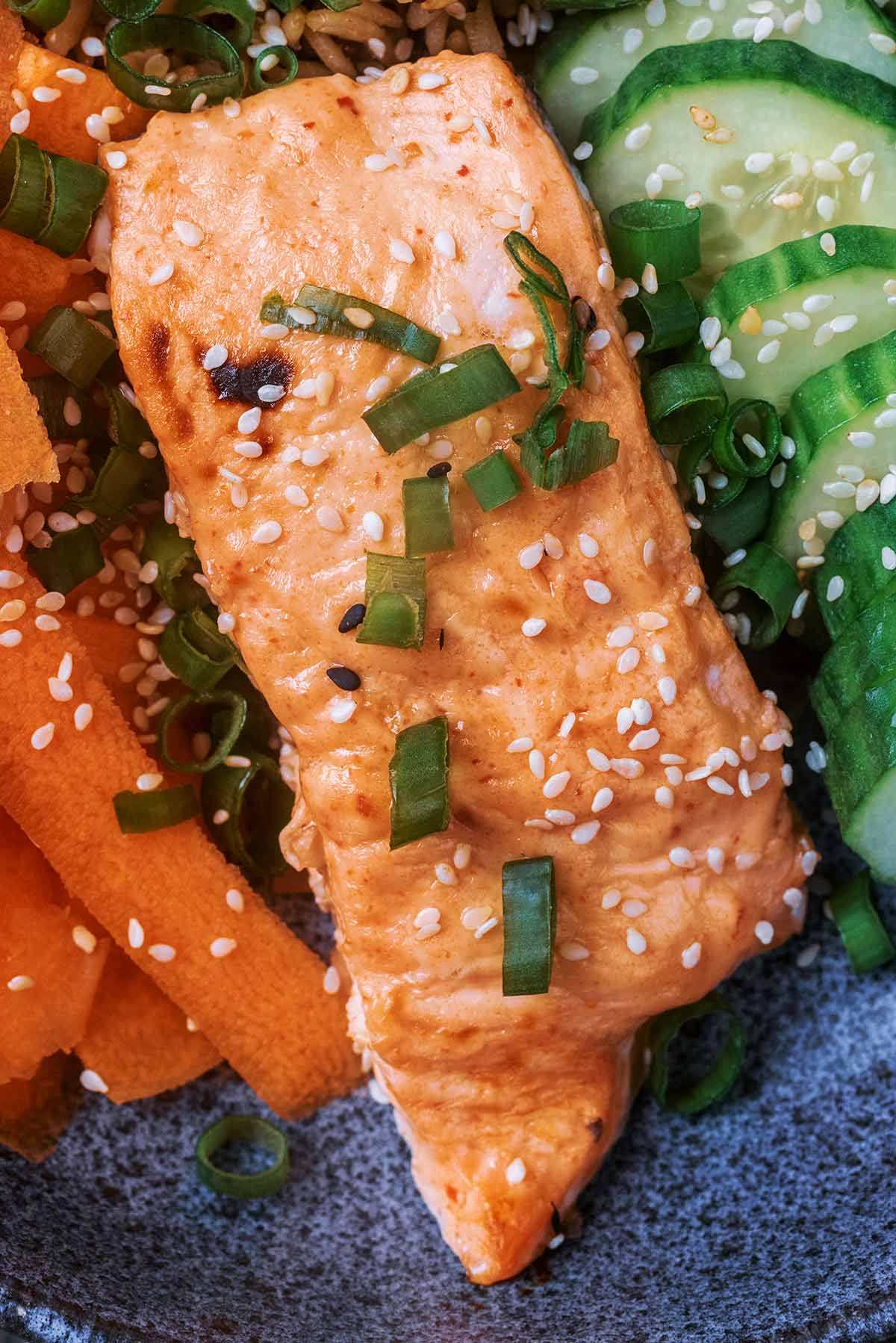 A cooked salmon fillet topped with sliced spring onions and sesame seeds.