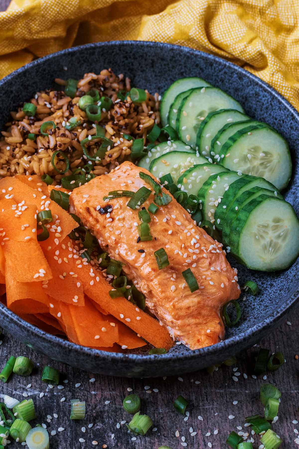 A bowl of salmon, rice and vegetables in front of a yellow towel.