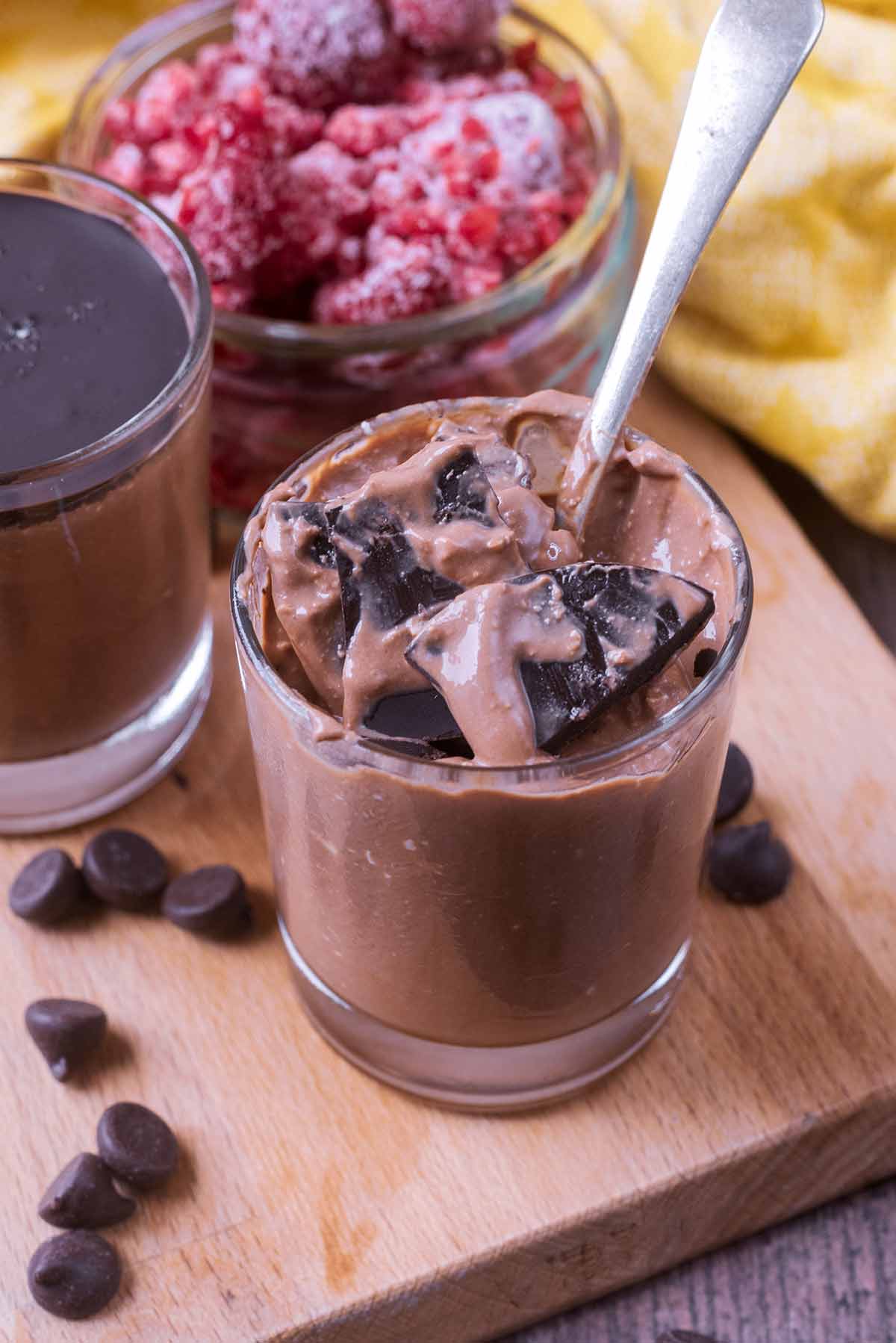 A spoon pushed through a layer of chocolate into a glass of chocolate mousse.