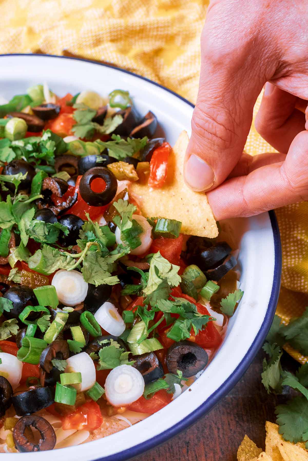 A hand dipping a tortilla chip into some loaded dip.