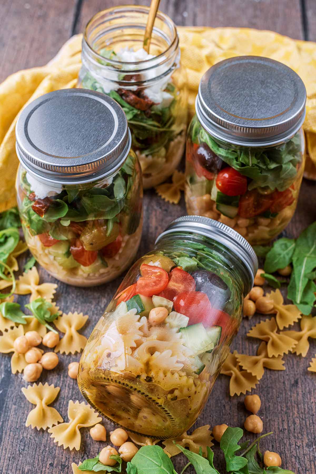 Four jars of pasta salad, one laying down and one with the lid off.