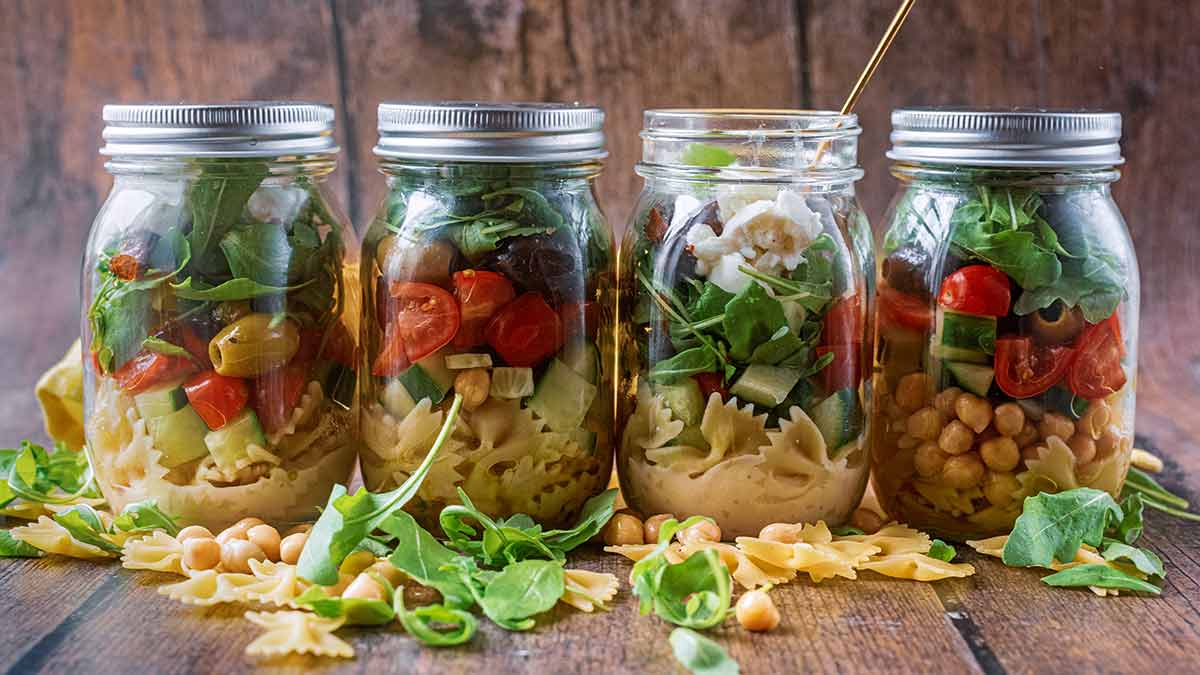 A row of four pasta salad jars stood in front of a wooden background.