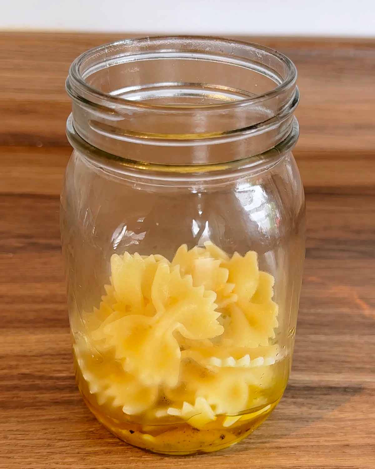 A jar with salad dressing and cooked pasta shapes in the bottom.