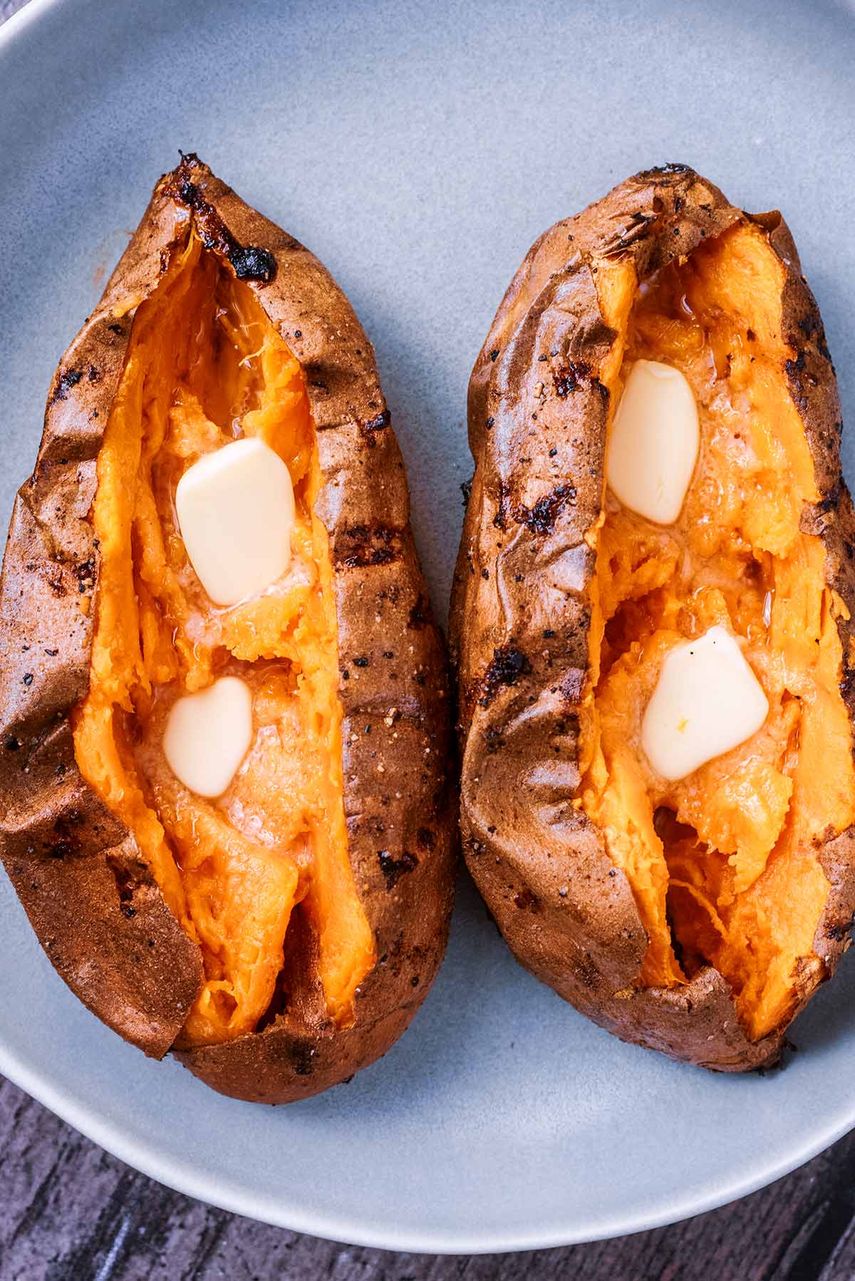 Two baked sweet potatoes cut open with melting butter in them.