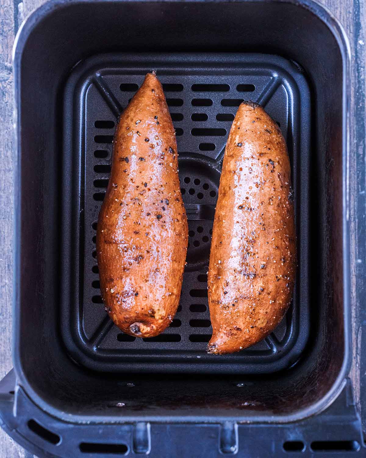 Two sweet potatoes in an air fryer basket.