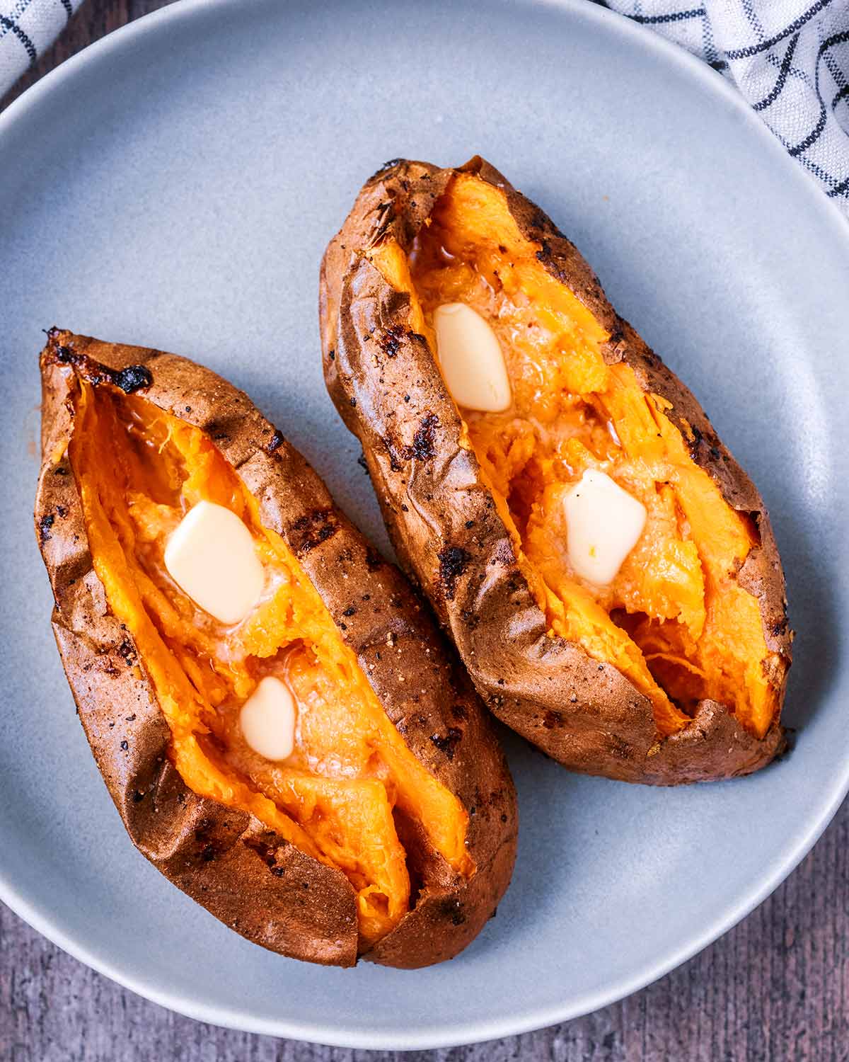 Cooked sweet potatoes, cut open with pats of butter melting in them.