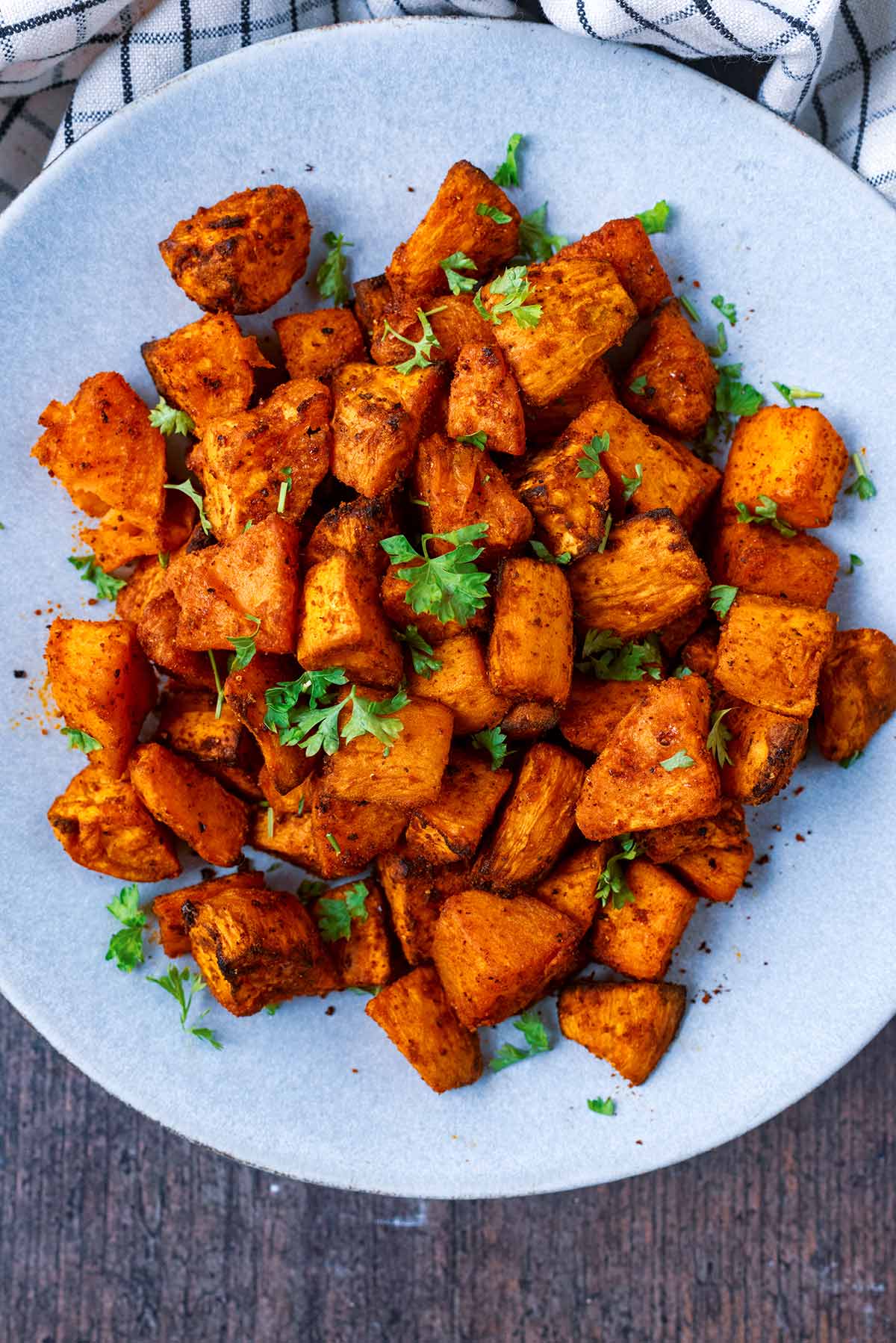 A plate of cooked cubed sweet potato on a wooden surface.