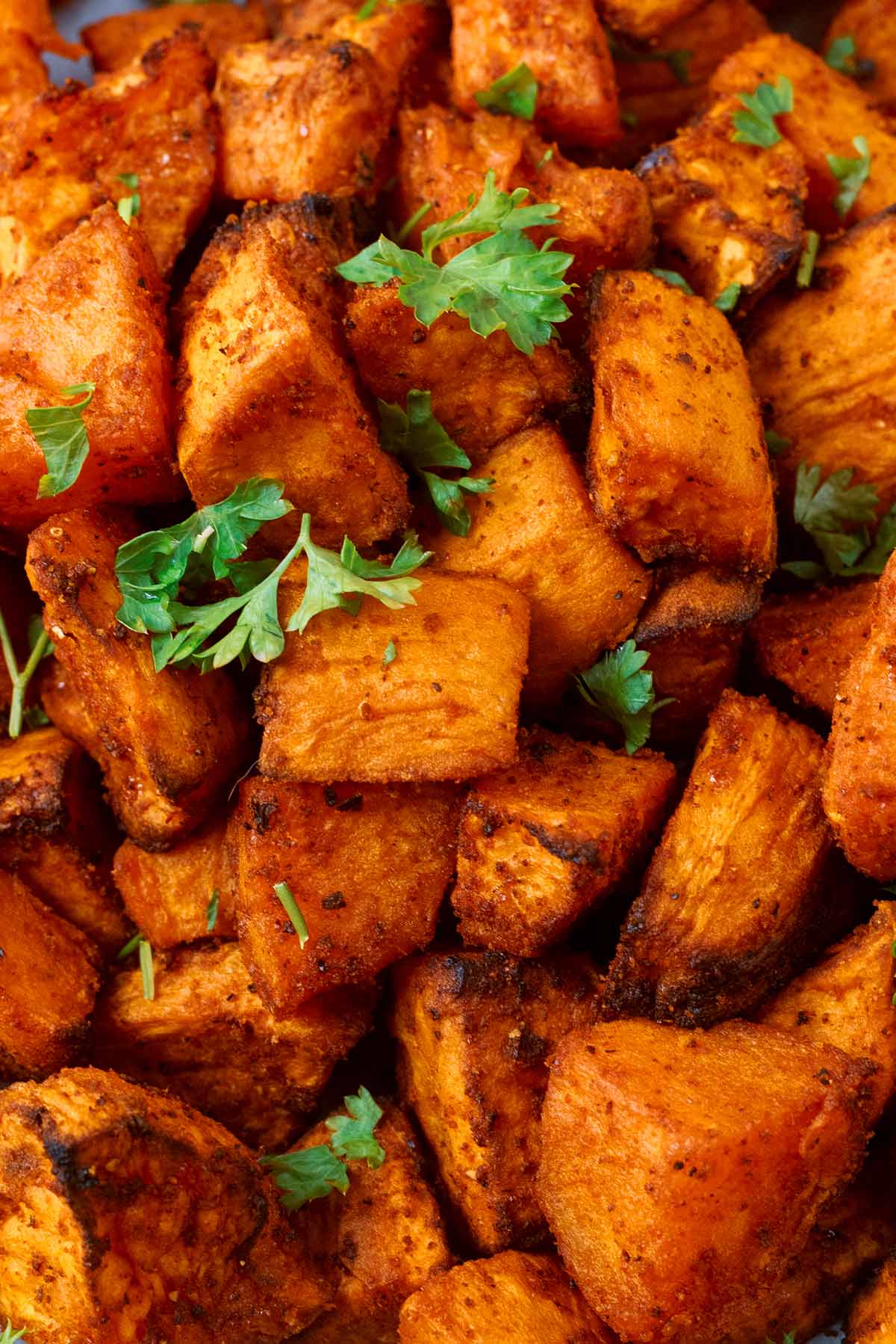 Cooked sweet potato chunks topped with fresh parsley leaves.