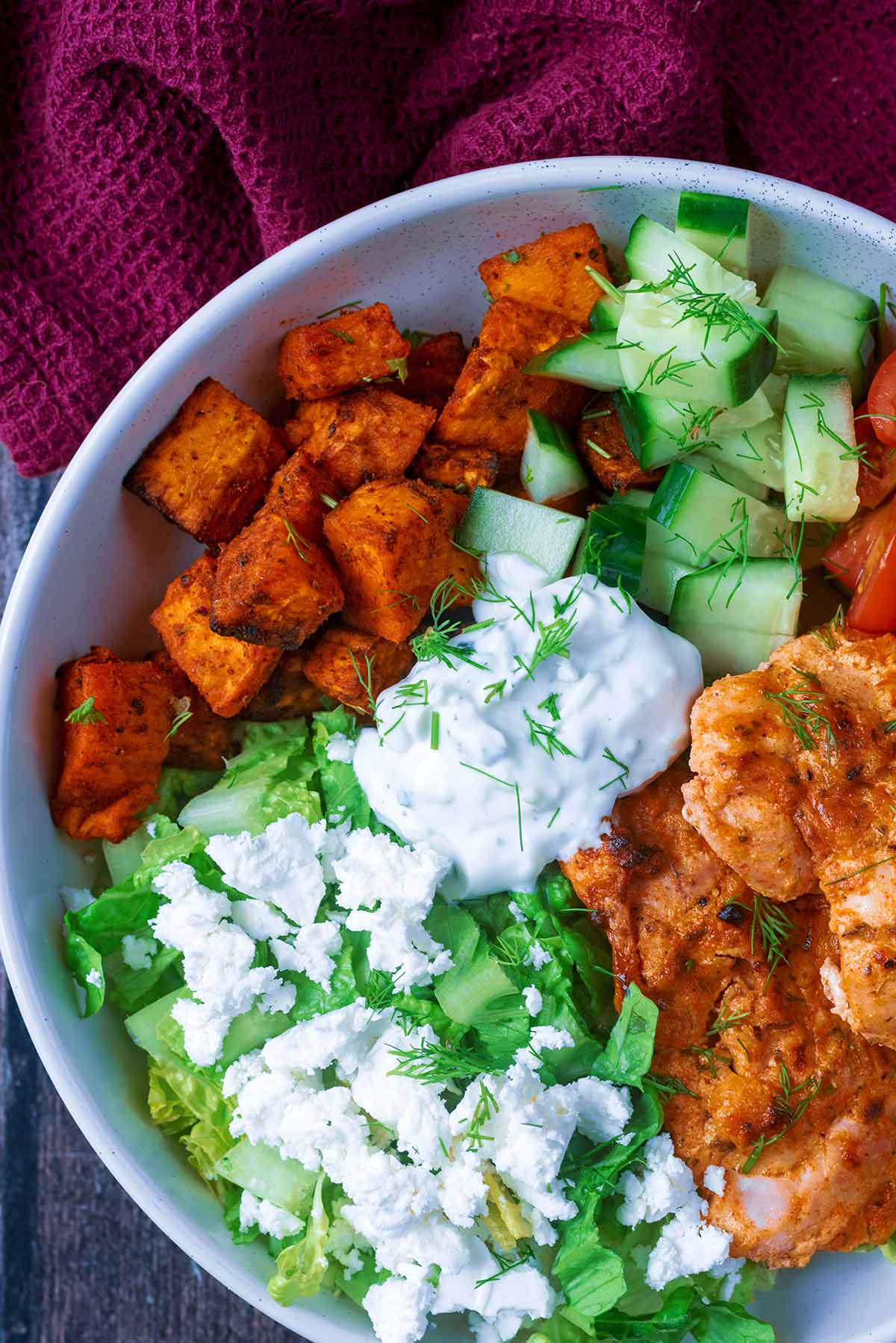 A bowl of cooked chicken, sweet potato, lettuce, cucumber, feta and tzatziki.