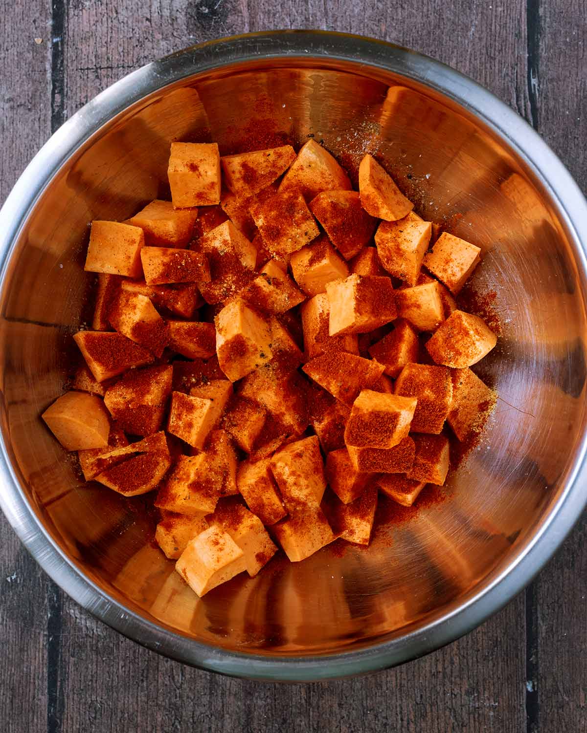 Sweet potato cubes in a bowl with oil and seasoning.