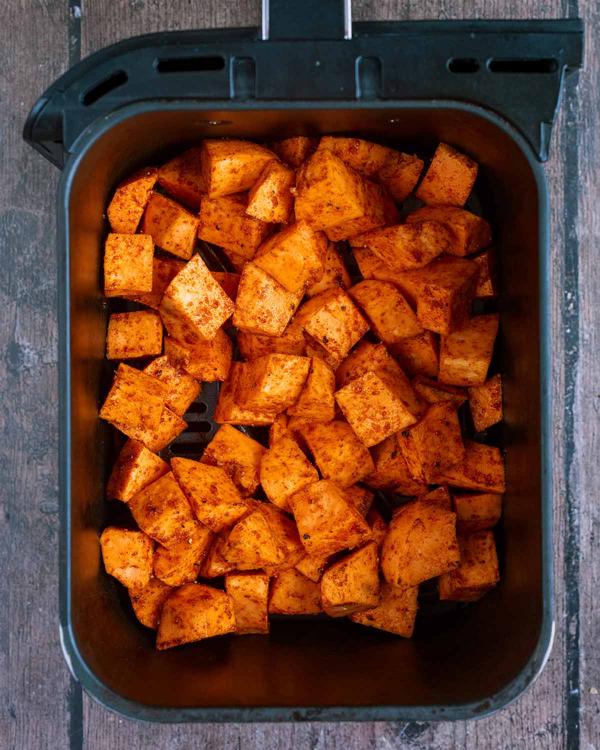 Seasoned sweet potato cubes in an air fryer basket.