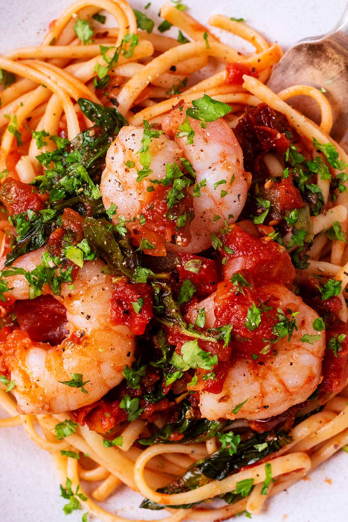 Three cooked king prawns on a bed of cooked linguine in a tomato sauce.