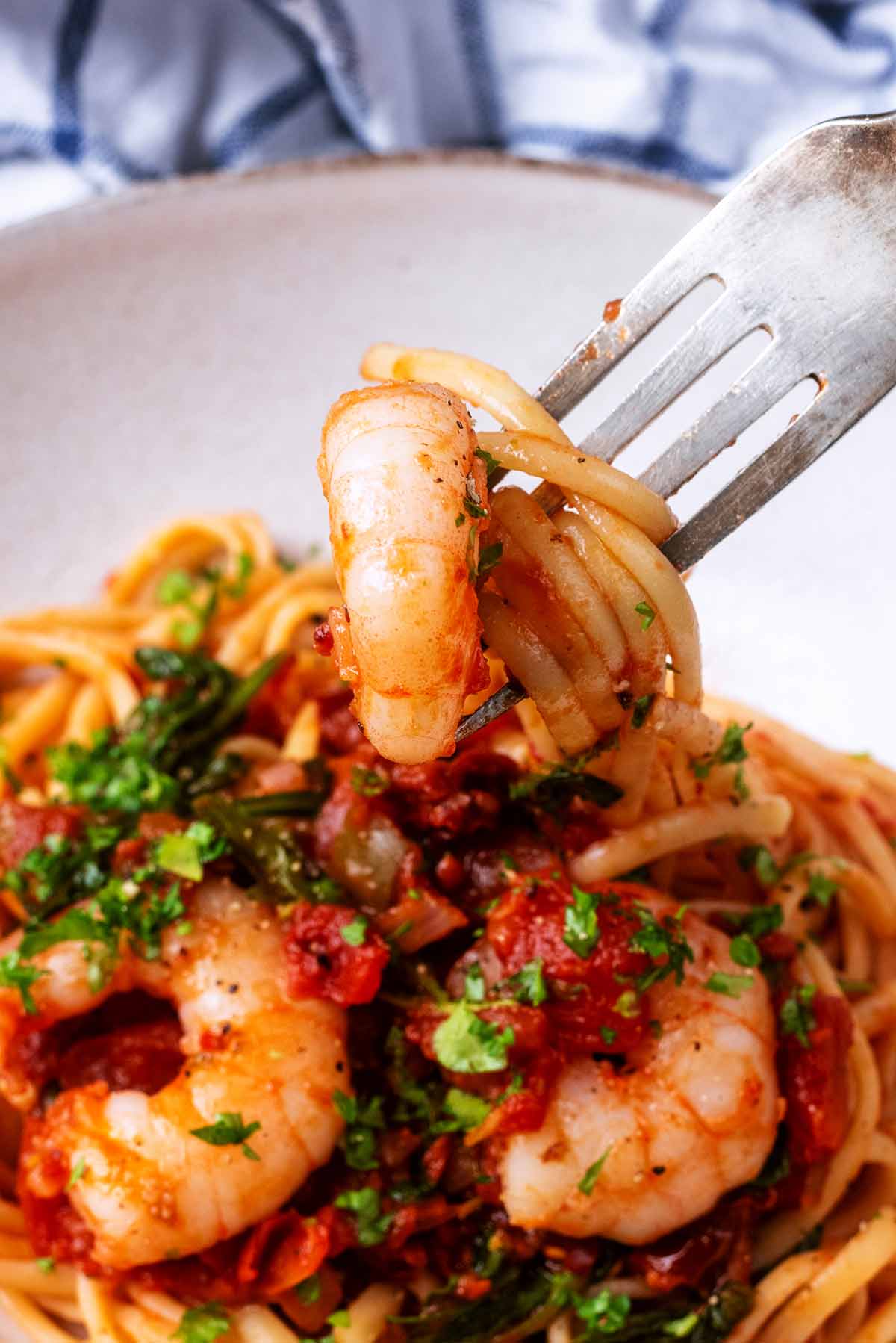 A fork lifting a cooked prawn and some linguine from a bowl.