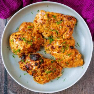 Four Greek yogurt chicken thighs on a round plate.