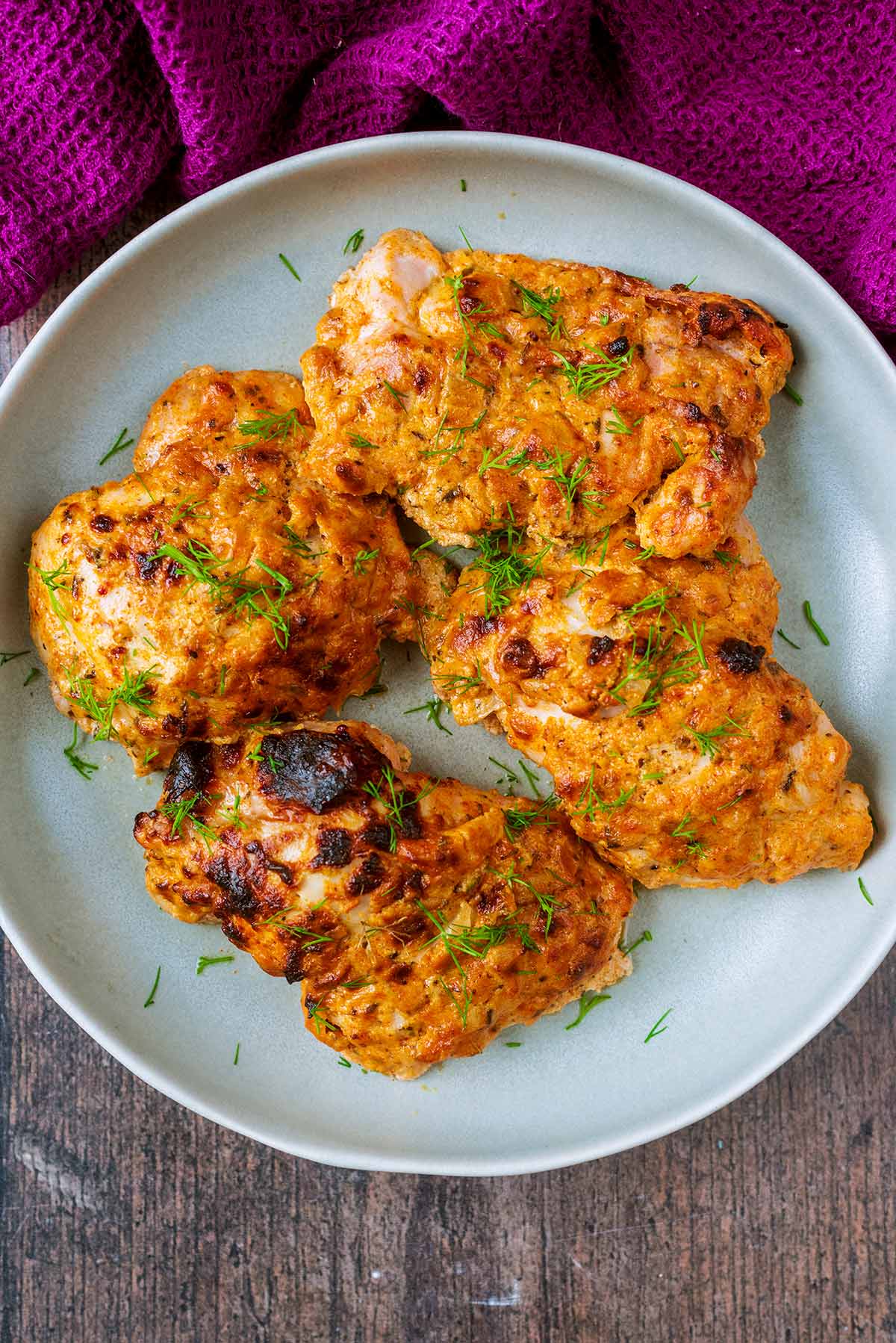 Four cooked coated chicken thighs on a plate next to a purple towel.