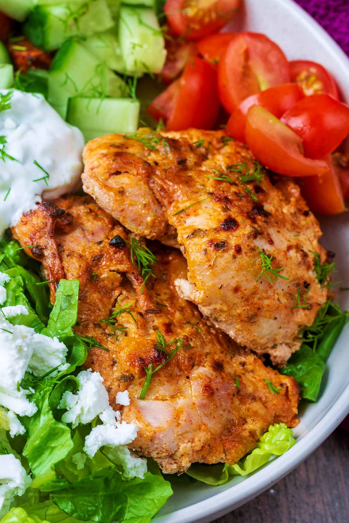 Two cooked Greek yogurt chicken thighs in a bowl with some salad.