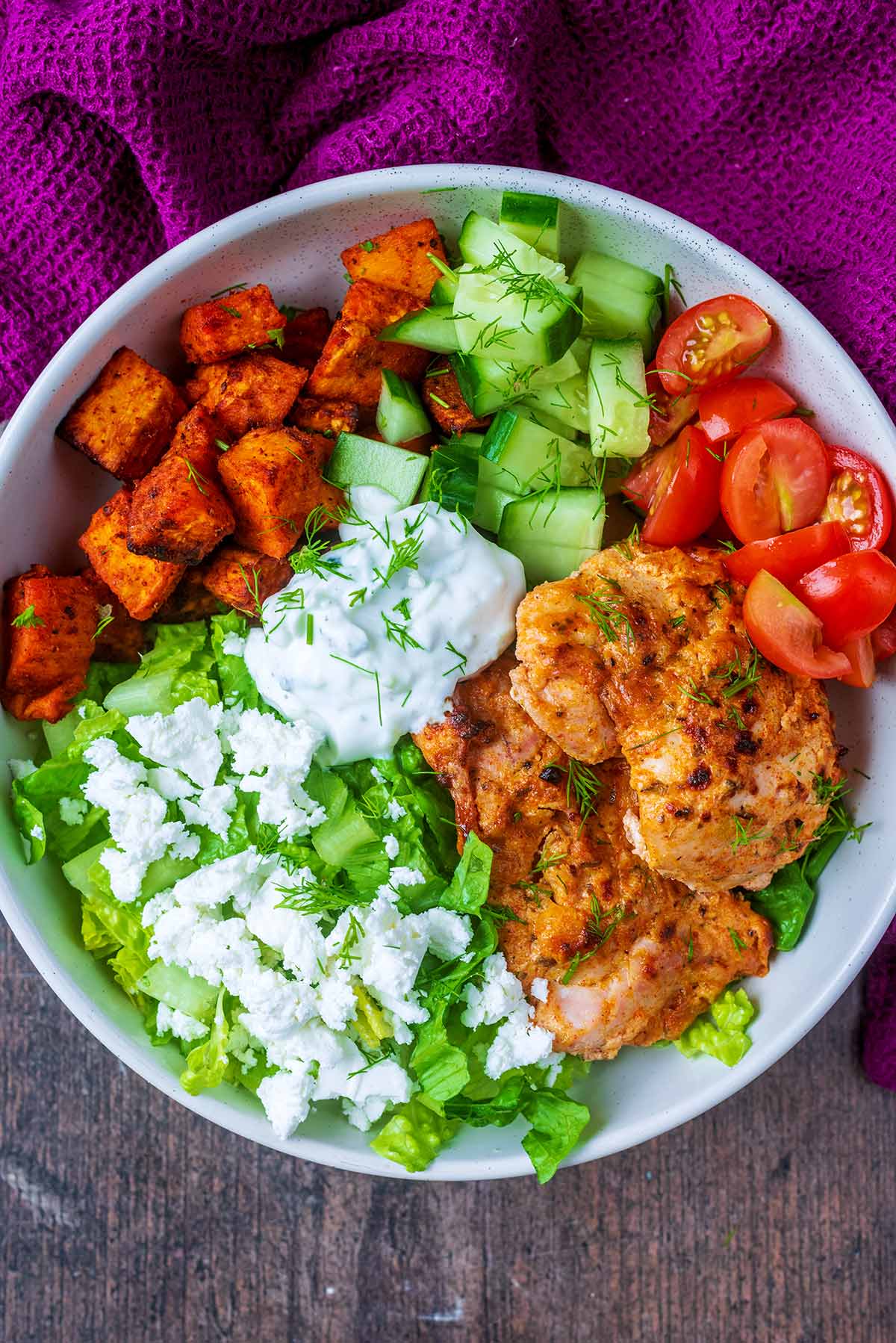 A bowl of chopped lettuce, cucumber, tomatoes, tzatziki and cooked chicken.