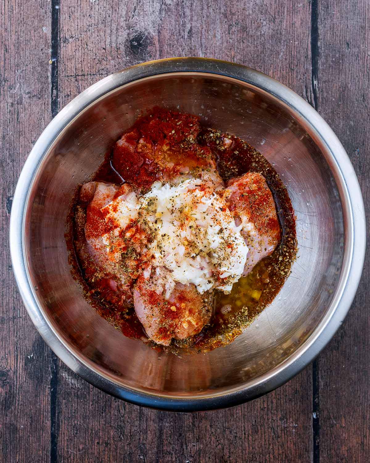 Chicken thighs, yogurt, herbs and spices in a mixing bowl.