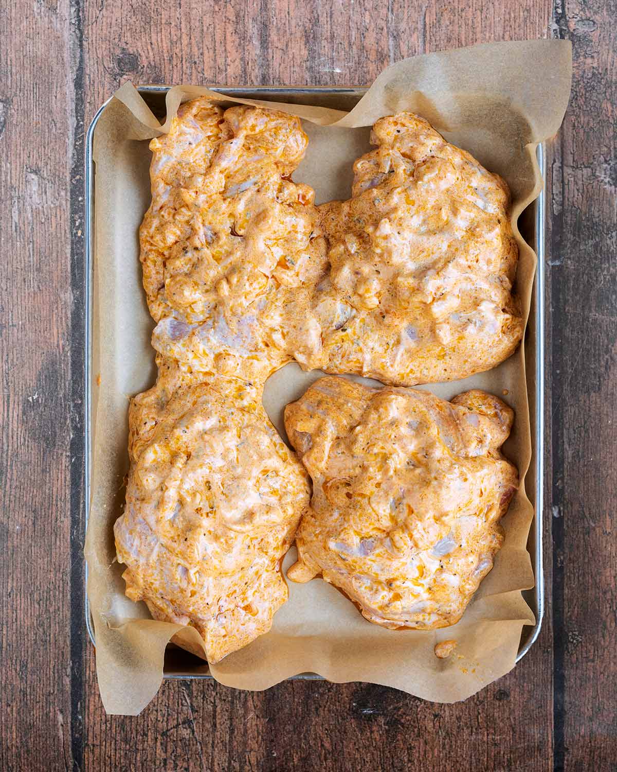 Coated chicken thighs on a lined baking tray.