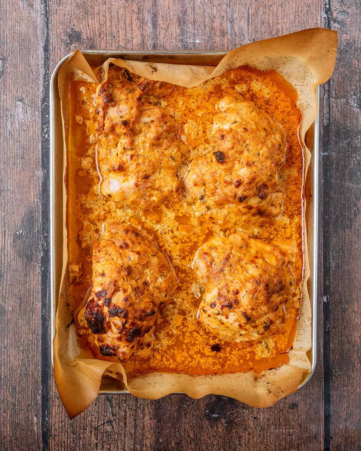 Coated and cooked chicken thighs on a lined baking tray.