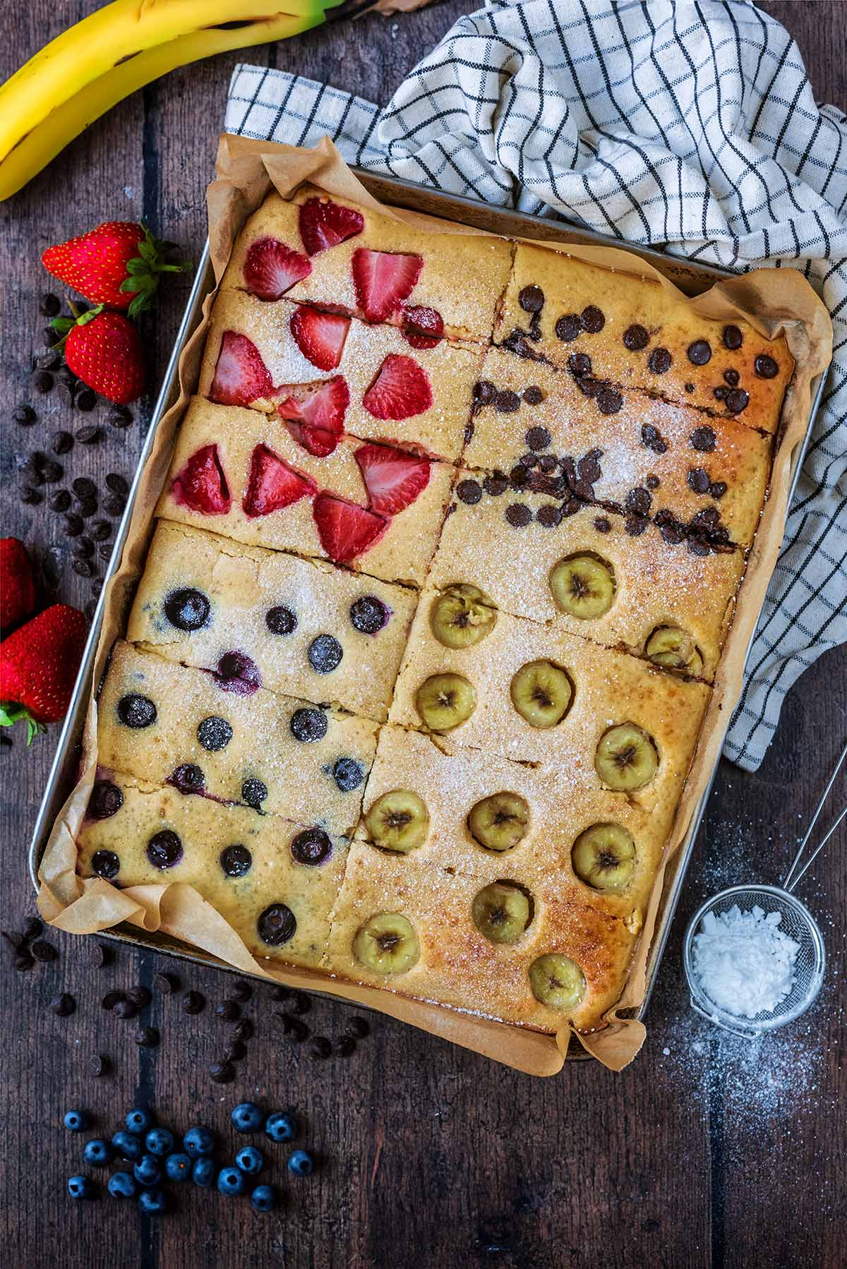 A tray full of baked pancakes topped with banana, strawberries, blueberries and chocolate chips. 