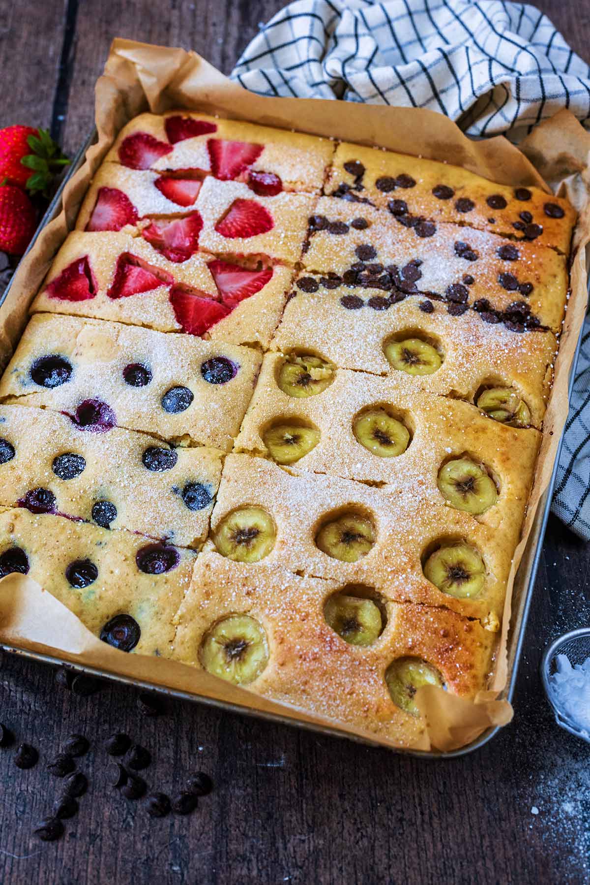 A tray of baked pancake on a wooden surface next to a checked towel.