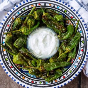 A bowl of air fryer padron peppers with a smaller bowl of creamy dip.