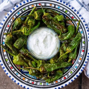 A bowl of air fryer padron peppers with a smaller bowl of creamy dip.