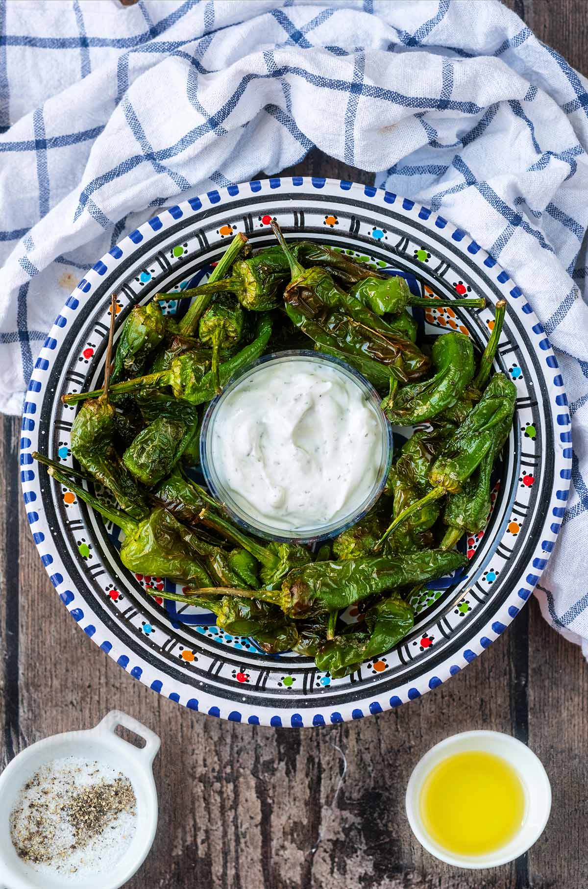 A bowl of cooked green chilli peppers with a pot of dip.