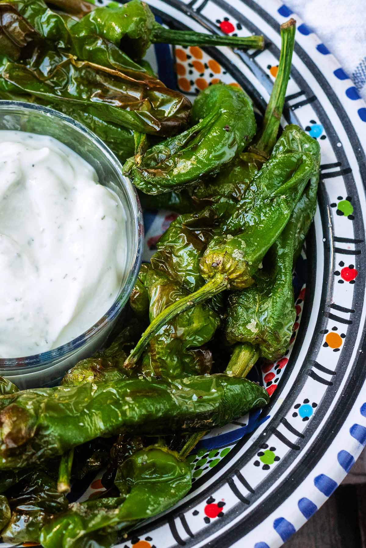 A small pot of creamy white dip next to cooked green peppers.