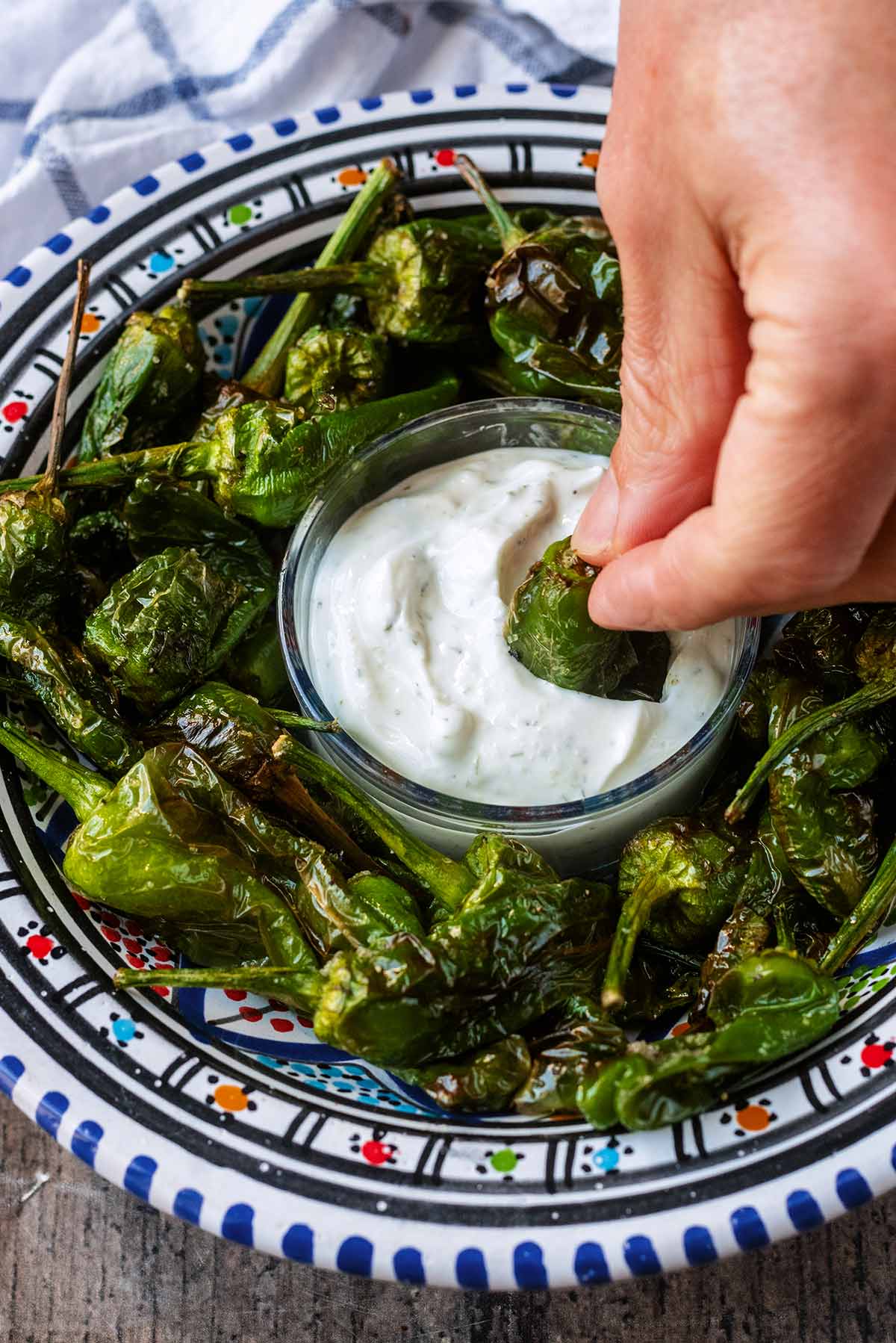 A hand dipping a cooked padron pepper into some dip.