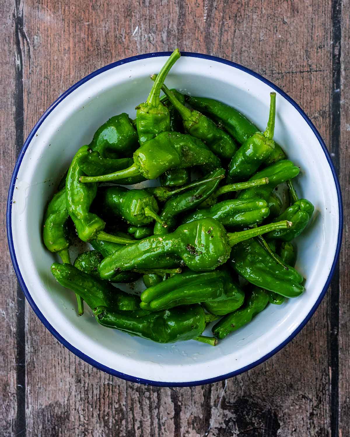 A bowl containing green peppers, oil and seasoning.